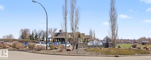 Entryway to Lewis Estates Golf Course featuring a stone and wood sign, mature landscaping, and a substantial parking area - 204 278 Suder Greens Drive, Edmonton, AB - Outdoor With View