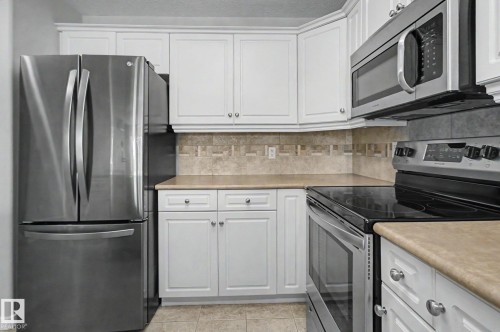 Kitchen featuring white cabinetry, stainless steel appliances, a tile backsplash, and light-toned countertops - 204 278 Suder Greens Drive, Edmonton, AB - Indoor Photo Showing Kitchen