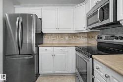 Kitchen featuring white cabinetry, stainless steel appliances, a tile backsplash, and light-toned countertops - 