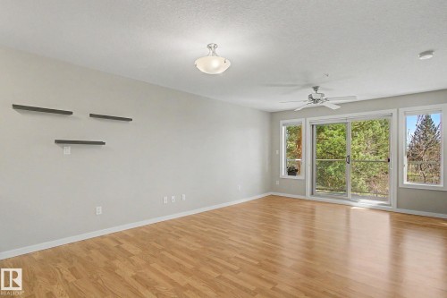 Spacious room featuring wood-finish flooring, light grey walls, and a multi-pane sliding glass door with side windows - 204 278 Suder Greens Drive, Edmonton, AB - Indoor Photo Showing Other Room
