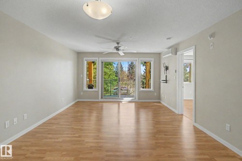 Bright living area featuring wood-finish flooring, a contemporary ceiling fan, and a ceiling-mounted light fixture - 204 278 Suder Greens Drive, Edmonton, AB - Indoor