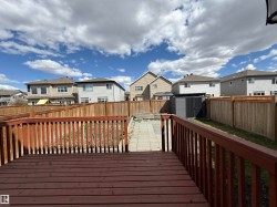 Expansive backyard featuring a stained wood deck, full privacy fencing, a paver stone walkway, and a modern storage shed - 
