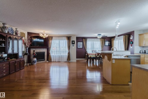 Open-concept living space featuring wood-finish flooring, a built-in fireplace with a tile surround and mantel, and a kitchen island with a stone countertop - 1764 Melrose Crescent, Edmonton, AB 