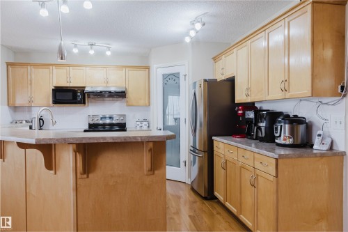 Kitchen featuring light wood cabinetry, stainless steel appliances, a center island with bar seating, and track lighting - 1764 Melrose Crescent, Edmonton, AB 