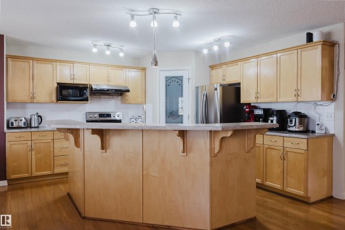 Kitchen featuring an angular island, abundant wood cabinetry, stainless steel appliances, and wood-finish flooring - 1764 Melrose Crescent, Edmonton, AB 