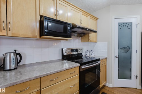 Kitchen featuring a built-in microwave, wood cabinetry, a stainless steel range with a ventilation hood, a tile backsplash, and a pantry door with frosted glass - 1764 Melrose Crescent, Edmonton, AB 