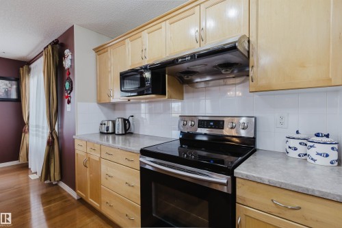 Kitchen featuring light wood cabinetry, stainless steel range with overhead microwave, grey-toned countertops, and white subway tile backsplash - 1764 Melrose Crescent, Edmonton, AB 