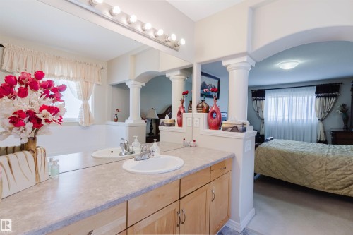 Spacious bathroom vanity featuring dual sinks, a large mirror with integrated lighting, light-toned wood cabinetry, and a neutral countertop - 1764 Melrose Crescent, Edmonton, AB 
