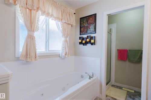 Soaking tub featuring integrated jets, a window with frosted glass, and polished chrome fixtures - 1764 Melrose Crescent, Edmonton, AB 