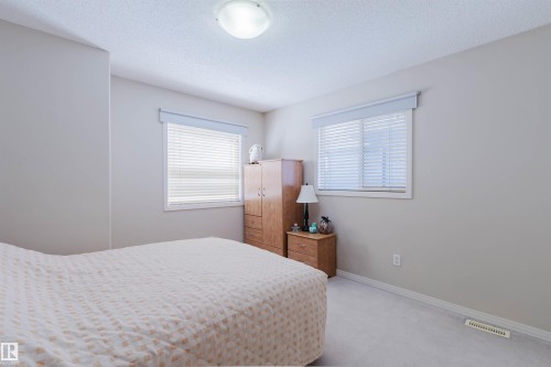 Carpeted bedroom featuring two windows with white blinds, light-colored walls, and a ceiling-mounted light fixture - 1764 Melrose Crescent, Edmonton, AB 