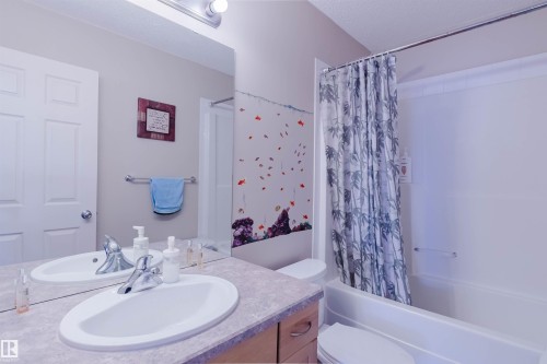 Bathroom featuring a vanity with an integrated basin, an expansive wall mirror, and a full bathtub with shower - 1764 Melrose Crescent, Edmonton, AB 