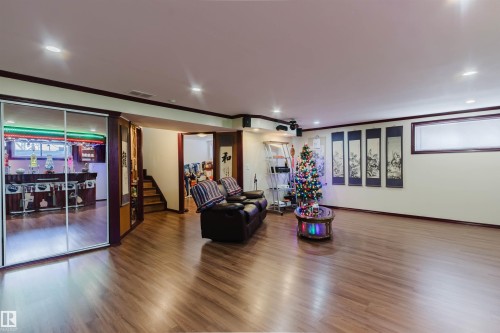 Lower-level entertainment space featuring wood-finish flooring, recessed lighting, and a mirrored wall reflecting a built-in bar - 1764 Melrose Crescent, Edmonton, AB 
