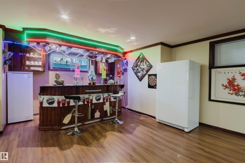 Dedicated bar area featuring wood-finish flooring, built-in cabinetry, recessed lighting, and a solid wood bar with integrated seating - 1764 Melrose Crescent, Edmonton, AB 