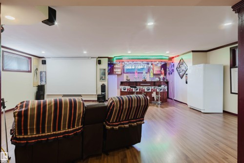 Entertainment room featuring a built-in wet bar with illuminated shelving, a large projection screen, wood-finish flooring, recessed ceiling lights, and perimeter accent lighting - 1764 Melrose Crescent, Edmonton, AB 