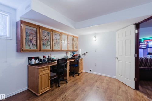 Wood-finish flooring throughout a versatile room featuring a built-in wood-finish desk with storage cabinetry - 1764 Melrose Crescent, Edmonton, AB 
