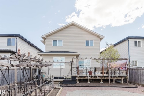 Rear exterior featuring a spacious wooden deck with decorative metal railings, a pergola structure, and a brick paver patio - 1764 Melrose Crescent, Edmonton, AB 