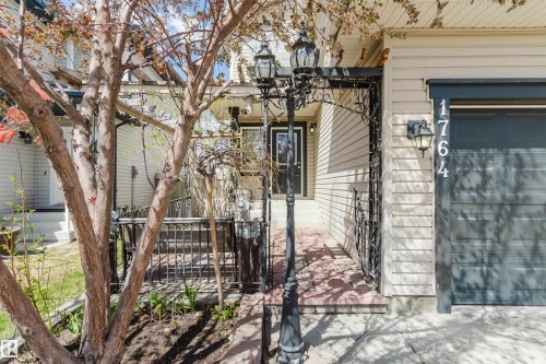 Front exterior with light-colored horizontal siding, a dark garage door, and decorative wrought iron accents - 1764 Melrose Crescent, Edmonton, AB 