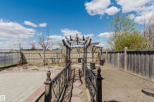 Outdoor pergola with an ornate metal railing, paver patio, and greenhouse structure - 1764 Melrose Crescent, Edmonton, AB 