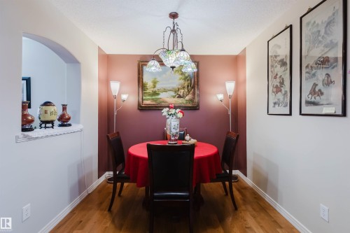 Dining area featuring a decorative chandelier with stained glass shades, wood-finish flooring, and an arched pass-through window - 1764 Melrose Crescent, Edmonton, AB 