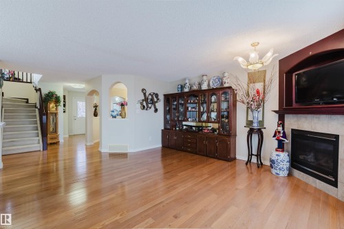 Expansive living area featuring wood-finish flooring, a built-in media center with a fireplace, a decorative ceiling light fixture, and a carpeted staircase with a wood railing - 1764 Melrose Crescent, Edmonton, AB 