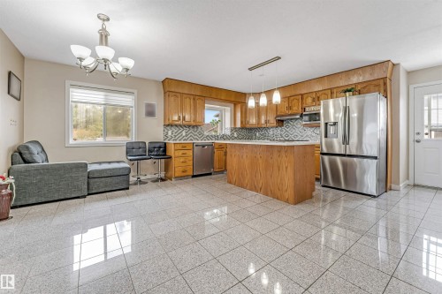 Spacious kitchen featuring a central island, wood cabinetry, stainless steel appliances, and a patterned tile backsplash - 1529 49A Street Nw, Edmonton, AB - Indoor Photo Showing Kitchen