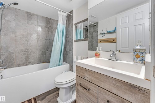 Full bathroom featuring a tub/shower combination with gray subway tile surround, a wood-finish vanity with an integrated sink, chrome faucet, and a large wall-mounted mirror - 1529 49A Street Nw, Edmonton, AB - Indoor Photo Showing Bathroom