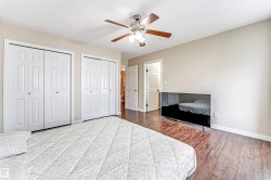 Bedroom with wood-finish flooring, two sets of bi-fold closet doors, and a ceiling fan with integrated lighting - 