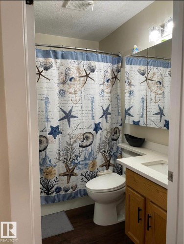Full bathroom featuring wood-finish flooring, a white toilet, and a light wood vanity with a white countertop and integrated sink - 1529 49A Street Nw, Edmonton, AB - Indoor Photo Showing Bathroom