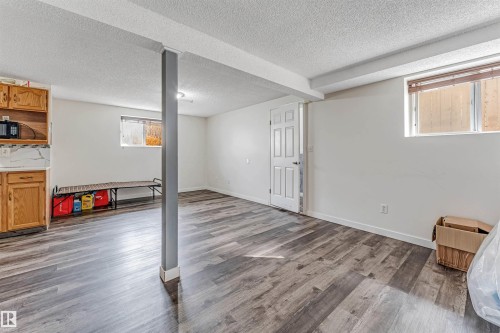 Spacious lower-level room featuring wood-finish flooring, white painted walls, and ceiling beams - 1529 49A Street Nw, Edmonton, AB - Indoor