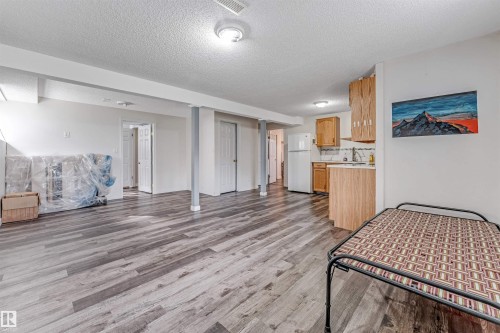 Open-concept living area with wood-finish flooring, recessed lighting, and a partial kitchen featuring wooden cabinetry and a white refrigerator - 1529 49A Street Nw, Edmonton, AB - Indoor