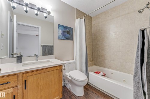 Bathroom featuring a wood-finish vanity with a white countertop, an undermount sink, and a rectangular mirror with a four-light fixture - 1529 49A Street Nw, Edmonton, AB - Indoor Photo Showing Bathroom