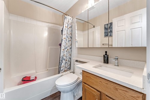 Bathroom featuring a white tub-shower combination, a wood-finish vanity with a light-toned countertop, an integrated sink with a chrome faucet, and a large medicine cabinet mirror - 1529 49A Street Nw, Edmonton, AB - Indoor Photo Showing Bathroom