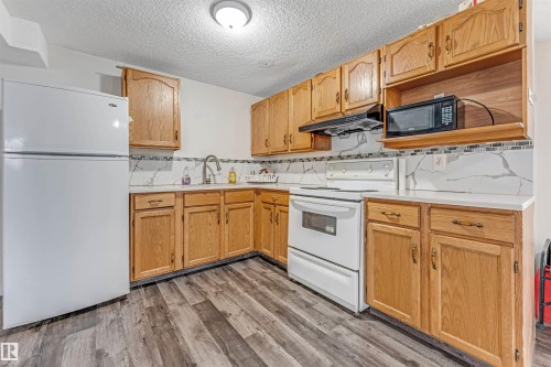 Kitchen featuring wood cabinetry, light countertops, wood-finish flooring, white appliances, and a tiled backsplash - 1529 49A Street Nw, Edmonton, AB - Indoor Photo Showing Kitchen With Double Sink