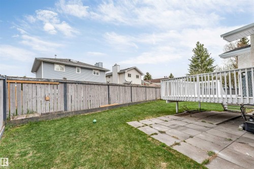 Expansive backyard featuring a manicured lawn, a raised wooden deck with white railing, and a patio area with stone pavers - 1529 49A Street Nw, Edmonton, AB - Outdoor