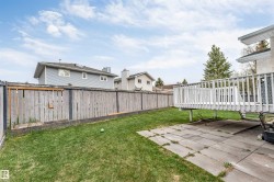 Expansive backyard featuring a manicured lawn, a raised wooden deck with white railing, and a patio area with stone pavers - 