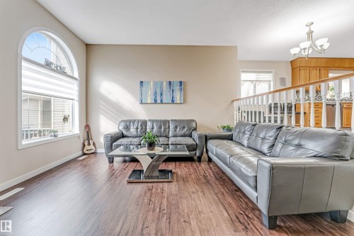 Spacious living area featuring wood-finish flooring, a large arched window with horizontal blinds, and neutral wall tones - 1529 49A Street Nw, Edmonton, AB - Indoor Photo Showing Living Room