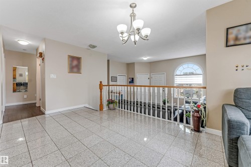 Polished tile flooring extending through the hallway, featuring a white spindle railing with wood-finish top rail, and an arched window - 1529 49A Street Nw, Edmonton, AB - Indoor Photo Showing Other Room