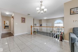 Polished tile flooring extending through the hallway, featuring a white spindle railing with wood-finish top rail, and an arched window - 
