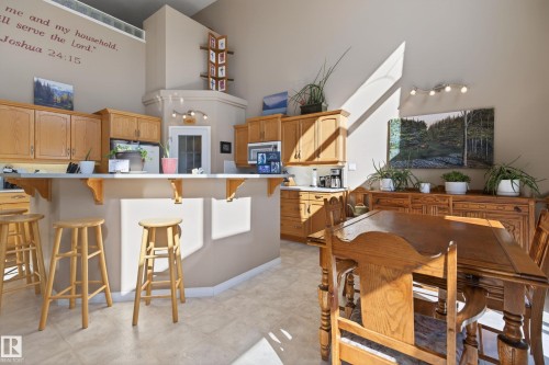 Kitchen and dining area featuring vaulted ceilings, wood cabinetry, a breakfast bar with an integrated countertop, and tiled flooring - 21 Pipestone Drive, Devon, AB - Indoor