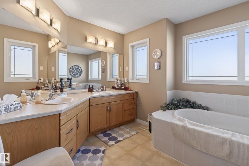 Bathroom featuring an integrated soaking tub with white tile surround, double vanity with light wood cabinetry, and large windows providing natural light - 21 Pipestone Drive, Devon, AB - Indoor Photo Showing Bathroom