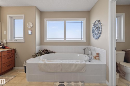 Soaking tub with a tiled surround, framed by multiple windows - 21 Pipestone Drive, Devon, AB - Indoor Photo Showing Bathroom
