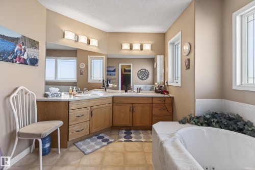 Spacious bathroom with dual vanities, wood-finish cabinetry, white countertops, and a built-in jetted tub - 21 Pipestone Drive, Devon, AB - Indoor Photo Showing Bathroom