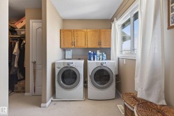 Dedicated laundry area featuring front-loading appliances, overhead wood-finish cabinetry, a large window, and carpet flooring - 