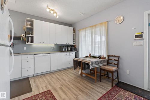 Kitchen featuring wood-finish flooring, white cabinetry, integrated dishwasher, and a window with sheer curtains - 21 Pipestone Drive, Devon, AB - Indoor