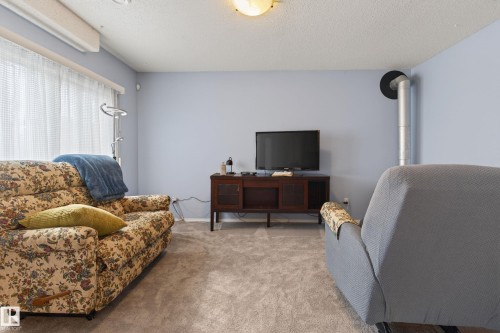 Carpeted living space featuring light blue walls, a large window with privacy blinds, and a built-in wall exhaust pipe - 21 Pipestone Drive, Devon, AB - Indoor