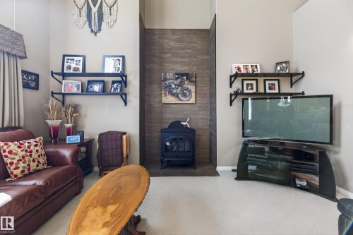 Living area featuring a floor-to-ceiling accent wall, a black freestanding stove, and plush carpeting - 21 Pipestone Drive, Devon, AB - Indoor
