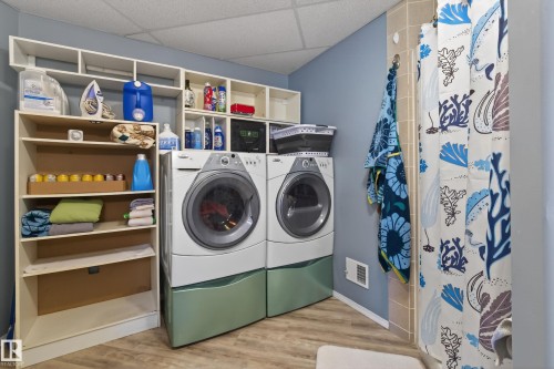 Dedicated laundry area featuring a washer and dryer set, wood-finish flooring, built-in shelving, and a tiled shower enclosure - 21 Pipestone Drive, Devon, AB - Indoor Photo Showing Laundry Room