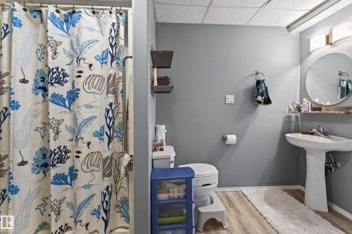 Full bathroom featuring a pedestal sink with a circular mirror, a toilet, and a shower area with a curtain - 21 Pipestone Drive, Devon, AB - Indoor Photo Showing Bathroom