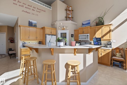 Kitchen featuring wood-finish cabinetry, a peninsula with a breakfast bar, white countertops, and light-colored flooring - 21 Pipestone Drive, Devon, AB - Indoor Photo Showing Kitchen