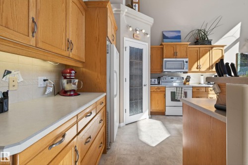 Kitchen featuring wood cabinetry, light-toned countertops, ceramic tile backsplash, and an integrated white appliance suite - 21 Pipestone Drive, Devon, AB - Indoor Photo Showing Kitchen
